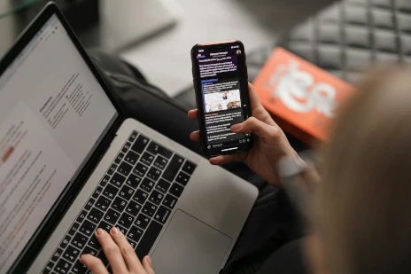 A laptop and mobile phone with someone appearing to be working on both simultaneously